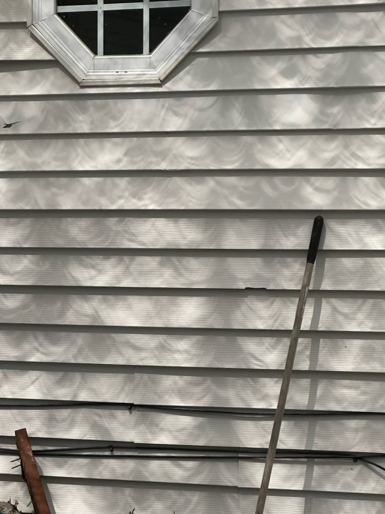 Twenty minutes before peak.  The siding of a white house is dappled with overlapping curved shadows.  They resemble giant rain drops.  The shadows point up.