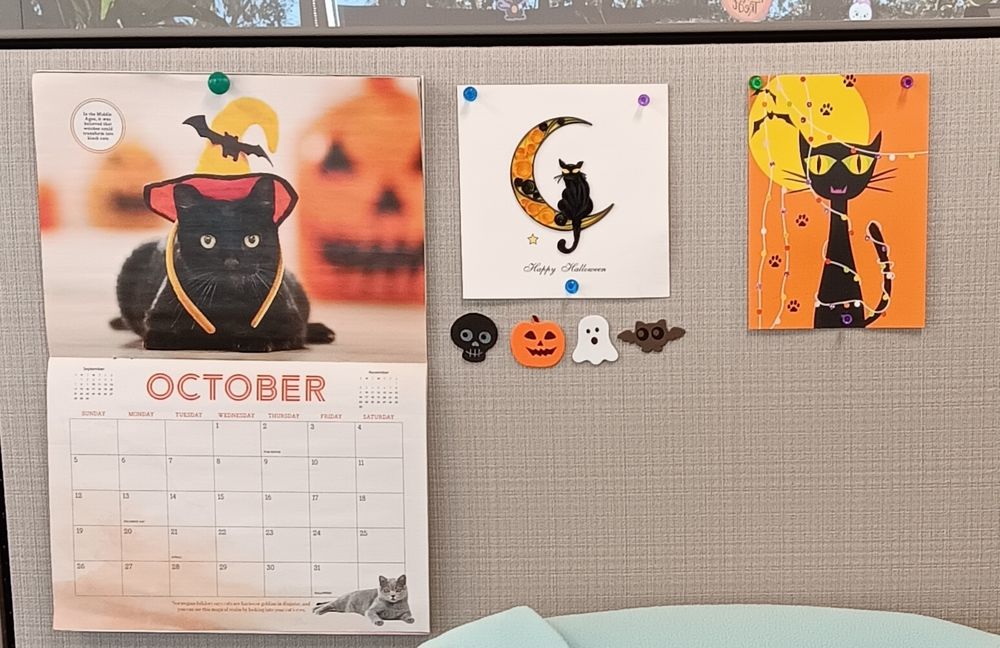 My wall at work features a Halloween calendar with a photo of a black cat wearing an orange witch hat and two Halloween cards with black cats on them. 