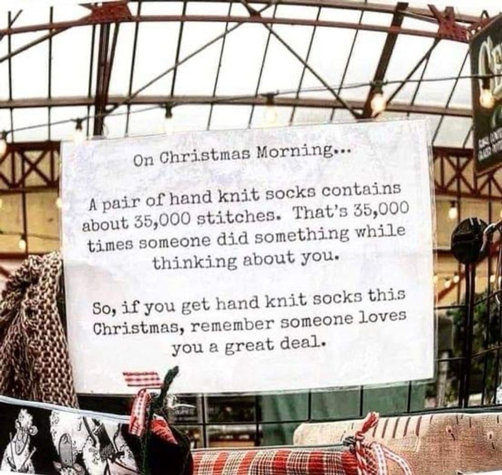 photo of a note card with a printed message on it, hanging in a space filled with handknit and handmade goods, under a glass roof.

"on Christmas morning...
a pair of hand knit socks contains about 35,000 stitches. That's 35,000 times someone did something while thinking about you.
So if you get hand knit socks this Christmas, remember someone loves you a  great deal.