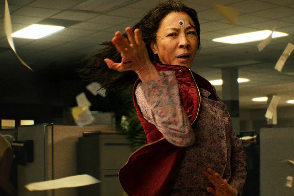 Michelle Yeoh as Evelyn Quan Wang in Everything Everywhere All At Once
A middle-aged Hong Kong woman, mid martial arts move. Hands moving into a defensive position across her body, head looking to the side, towards her leading arm. There are papers flying through the are. Her face is streaked with blood, hair flowing, a look of concentration on her face, and one googly eye stuck in the middle of her forehead where most people think the third eye is.
She's in a fleece vest over a pink floral printed blouse.