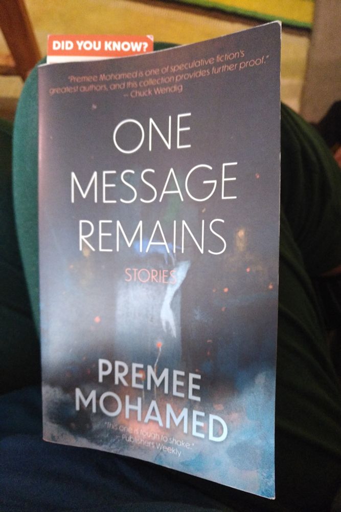 The paperback collection of Premee Mohamed's short stories One Message Remains.
The cover is a deep navy blue and looks like an oil painting.
There's a misty door in the middle and a pale hand reaching through from the darkness above. Small orange-red dots light up the darkness and a couple look like flowers growing from misty stems. From the pale mists along the bottom and the darkness all over, hollow-eyed heads and agonized specters emerge.

Two quotes:
"Premee Mohamed is one of speculative fiction's greatest authors and this collection provides further proof." - Chuck Wendig
"This one is tough to shake." - Publishers Weekly.
