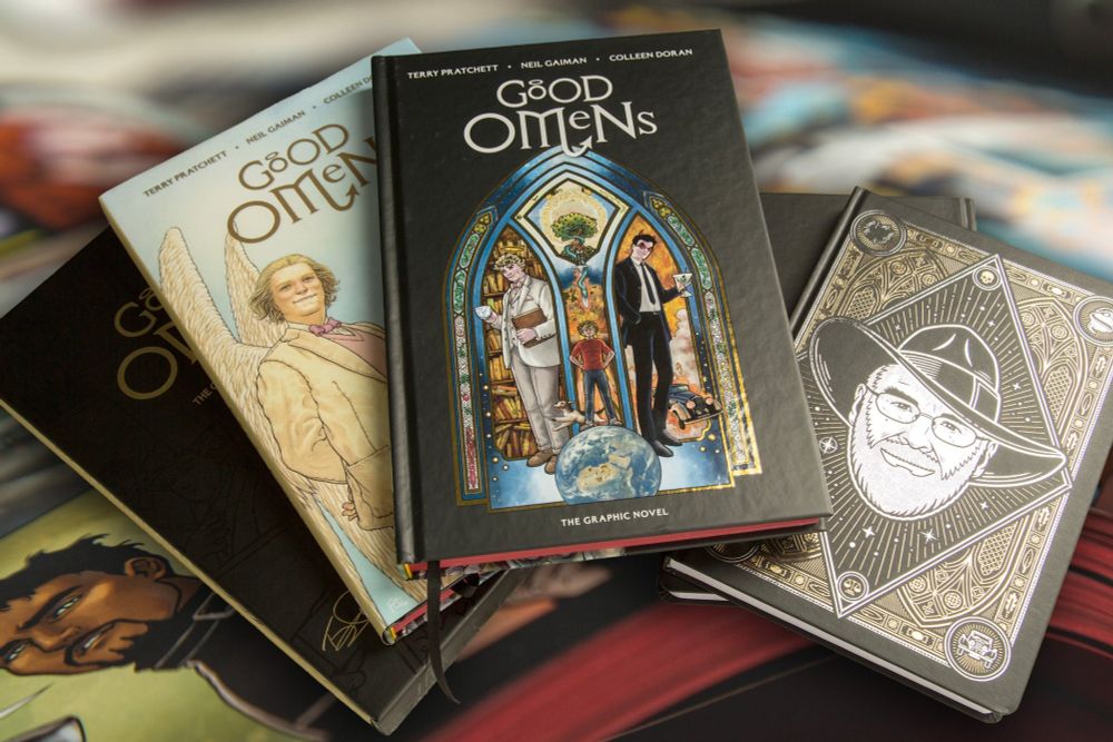 A selection of the rewards from the Good Omens Kickstarter, including different editions of the graphic novel, the dust jacket, the slipcased edition and an author notebook showing Sir Terry Pratchett.