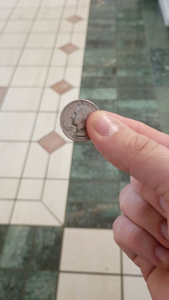 The picture of a hand holding one American quarter between an index finger and a thumb.