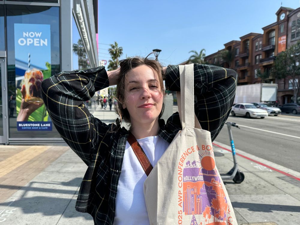 Woman standing on a street corner with her arms behind her head holding an AWP tote