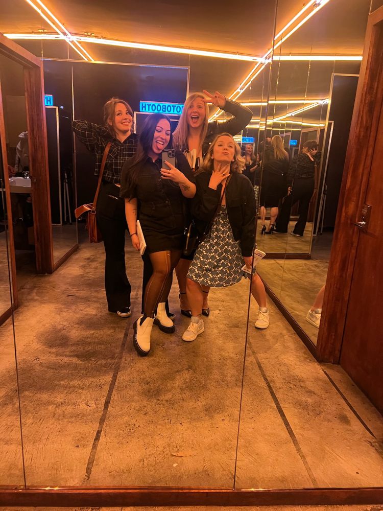 Group of 4 women posing in a lighted hallway near bathrooms 