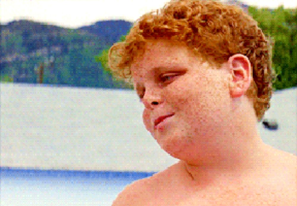 a shirtless boy with red hair and freckles looks to the side