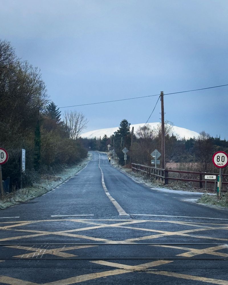 A road with a Hill in the background with snow cover