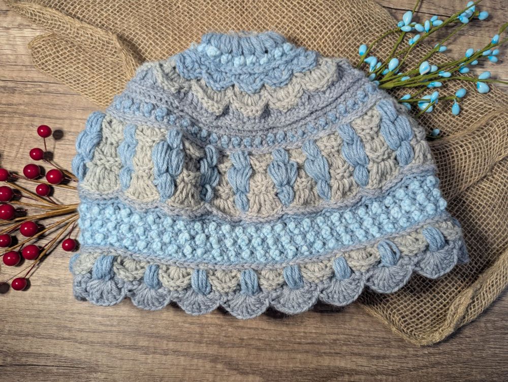 A crocheted hat in various blues and grays. The hat has shell and puff stitch motifs and is an example of colorwork in crochet 