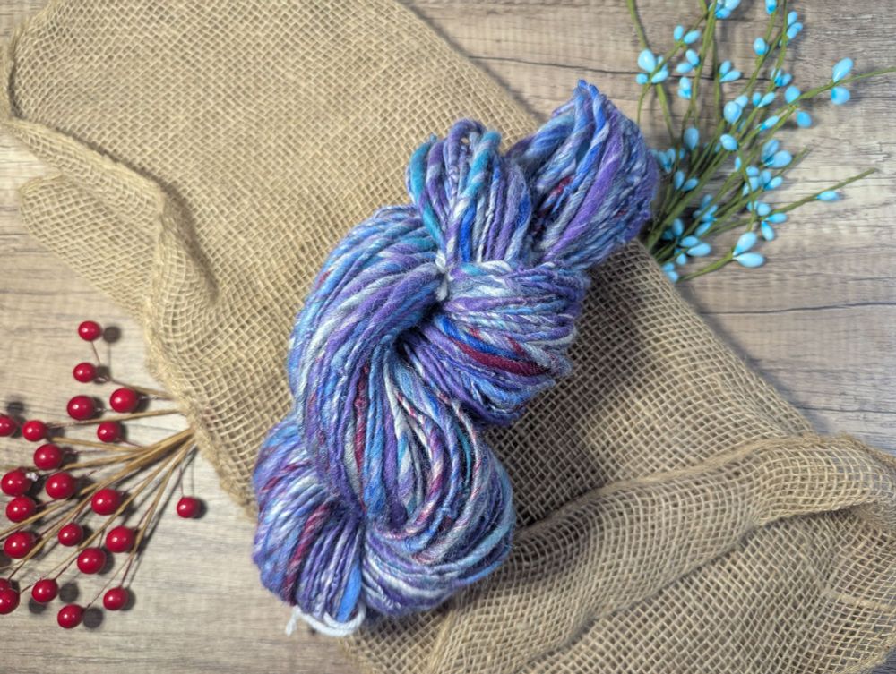 a hank of handspun yarn. the yarn is various shades of blue, purple, and dark pink marled with white.