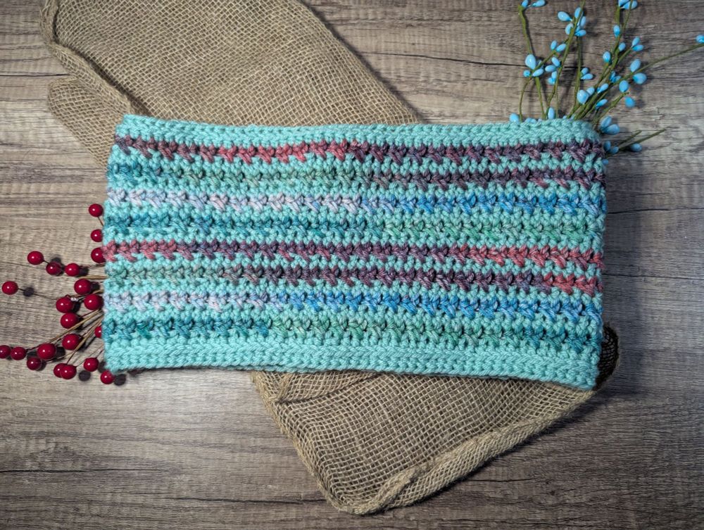 A crocheted cowl that is striped with mint and variegated yarn. 