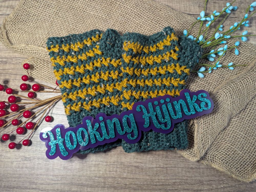 A crocheted pair of fingerless mitts. The mitts use dark green and gold tweed yarns. 