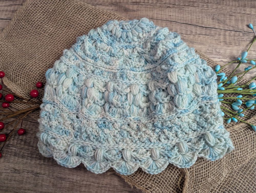A picture of a crocheted hat. The hat has intricate details and is done in a yarn that is blue and white variegated 