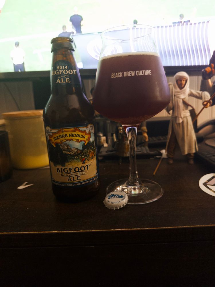 A glass and a bottle of 2014 Bigfoot in front of my tv and next to Dr.Jones. 