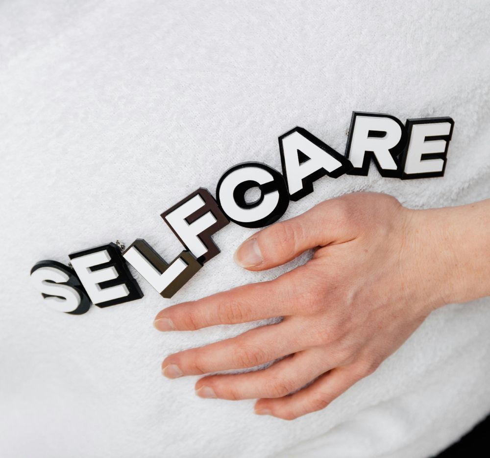 A close-up of a hand resting on a white towel with the word 'selfcare'.