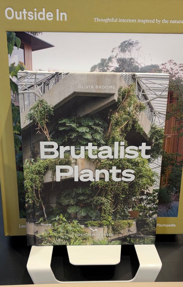 Books on display in the Geelong Art Gallery shop. Frontmost is “Brutalist Plants” with a cover photo of a 1970s-style concrete building festooned with assorted ferns, epiphytes, climbers and other verdant green plants.