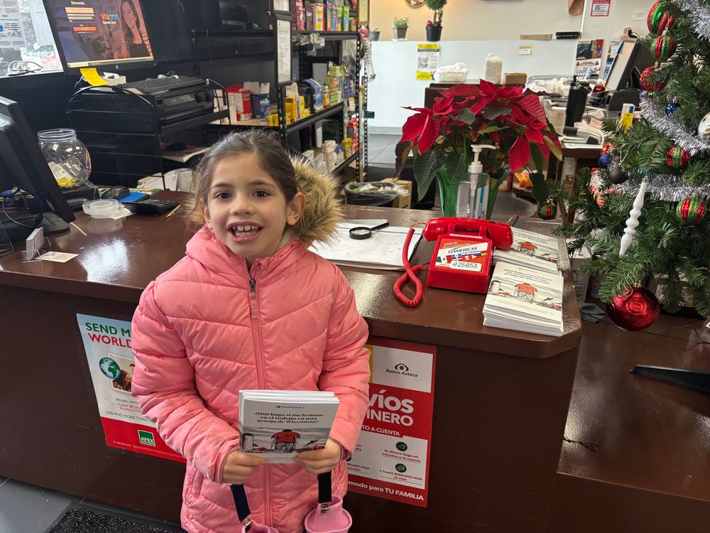 My beautiful kid holding some guides in front of an area where people can wire money to their home countries 