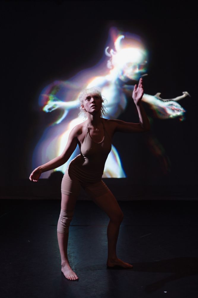 A female dancer performs with an AI generated avatar on the screen behind her