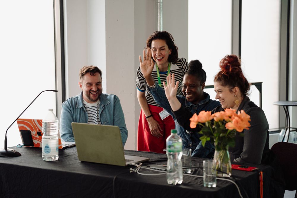 Four people - three women and a man - wave goodbye to someone on a laptop screen after a festival panel discussion
