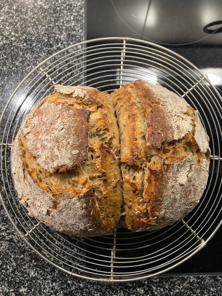 Sauerteigbrot mit Schnitt in der Mitte (damit es später gut zweigeteilt werden kann) auf einem runden Auskühlgitter auf Granitküchenablage.