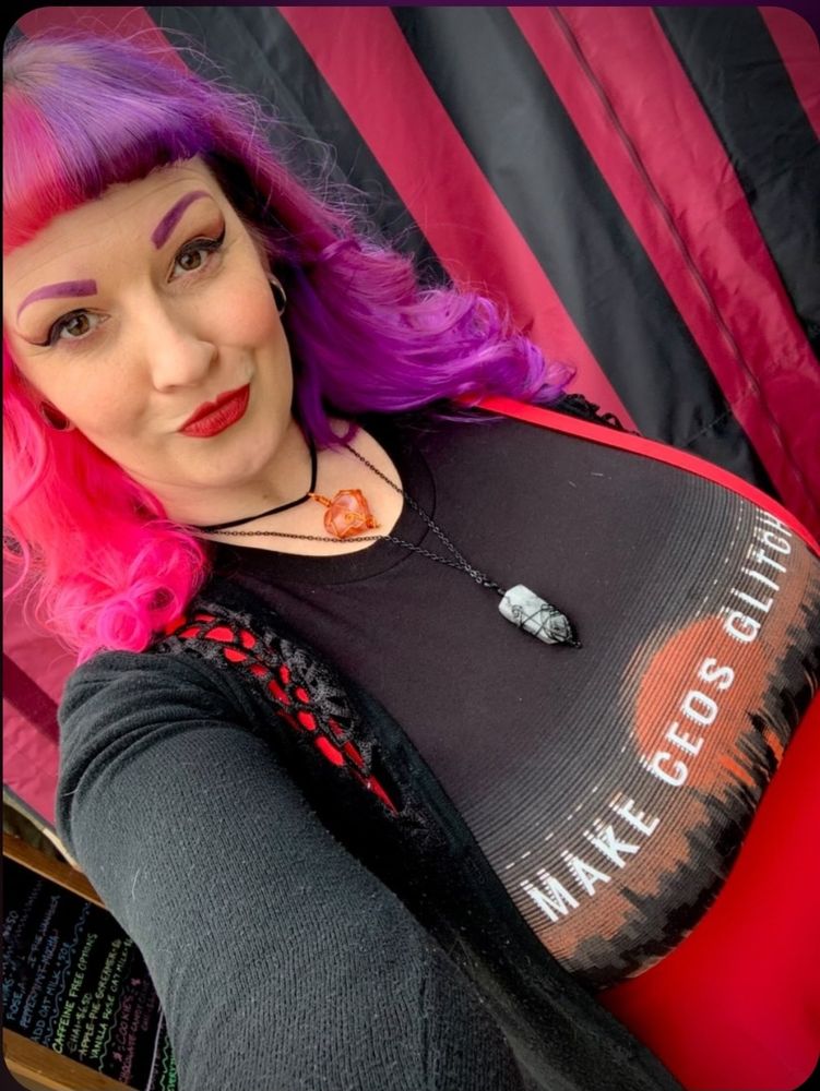 A fem person modeling a Make CEOS Glitch graphic tee, wearing a red & black outfit, in front of a red & white striped tent