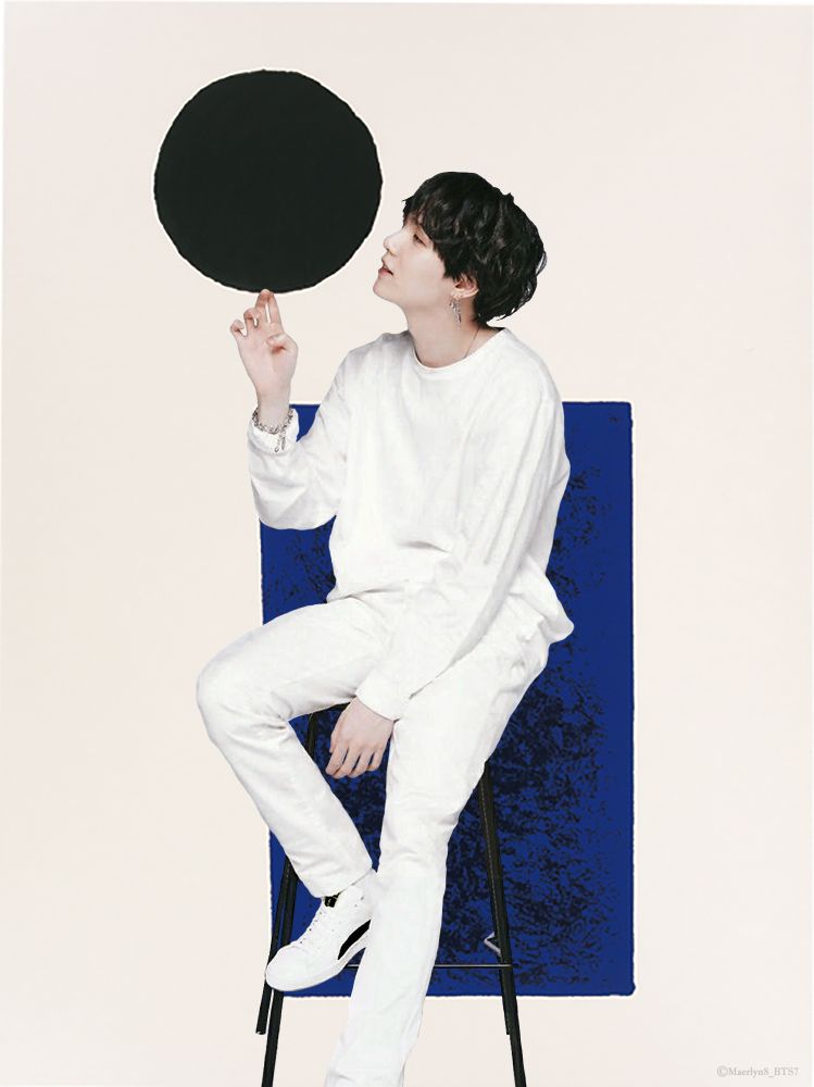 Yoongi in white with fluffy black hair, sitting on a stool, "spinning" a black circle on his fingers. 