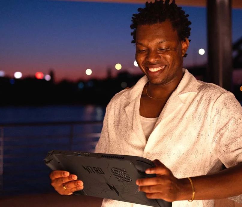 A Black person in a white shirt holds a massive handheld gaming PC