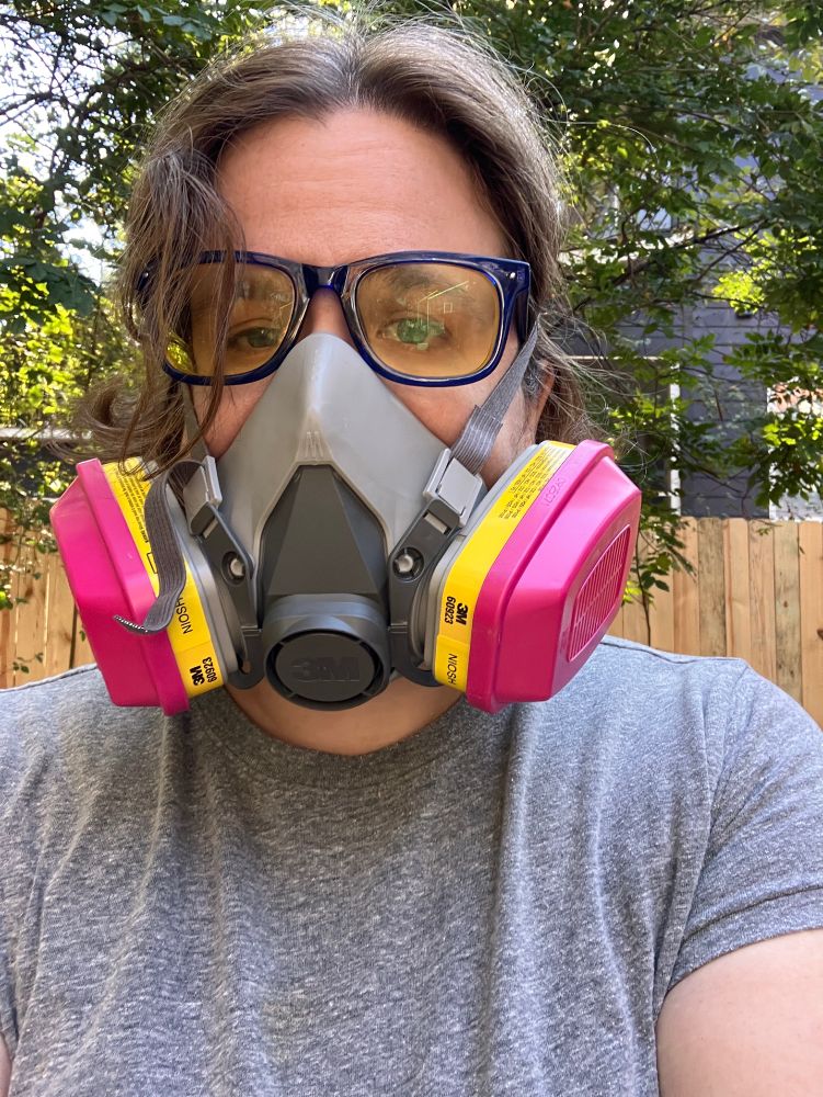 A woman in a gray shirt wearing a half mask respirator.