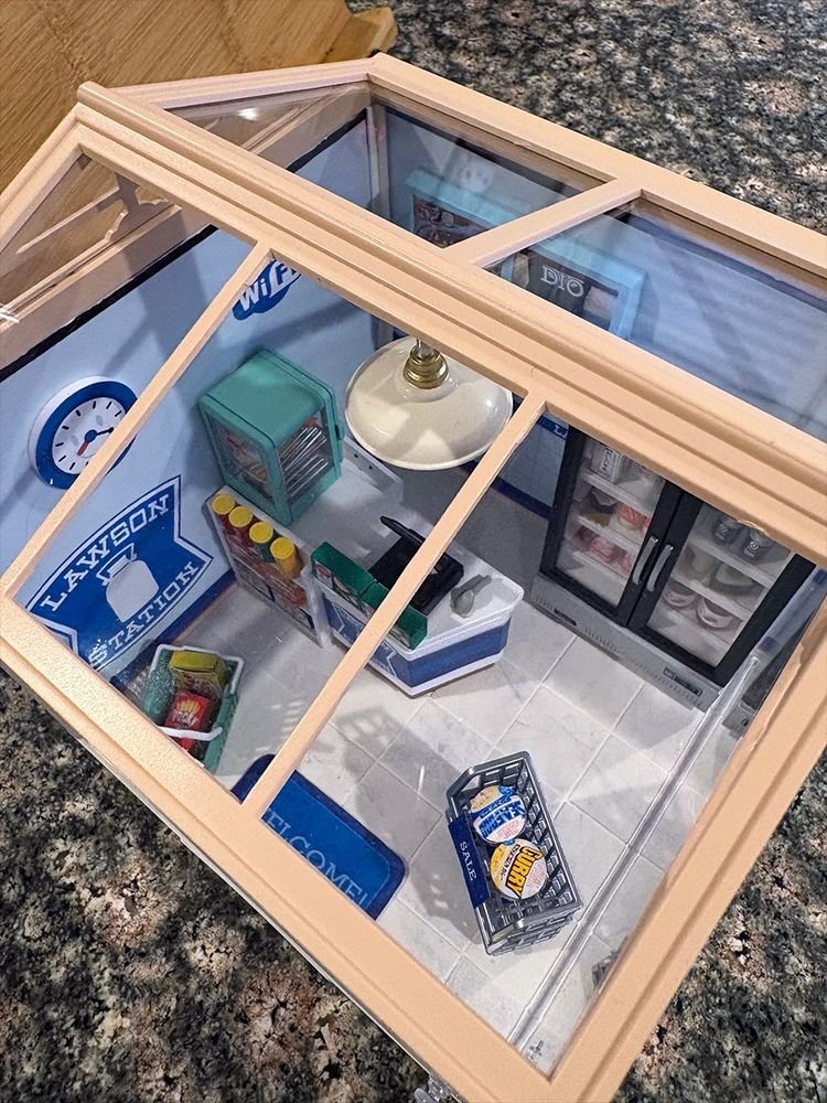 Top down close up of miniature Lawson convenience store. Details showing the small food on the shelves, counter, and in the freezer. 