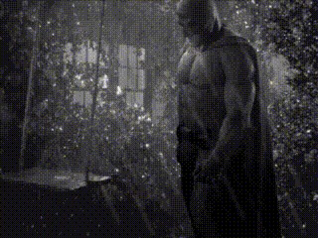 a black and white photo of a shirtless man in a cape standing in a room .