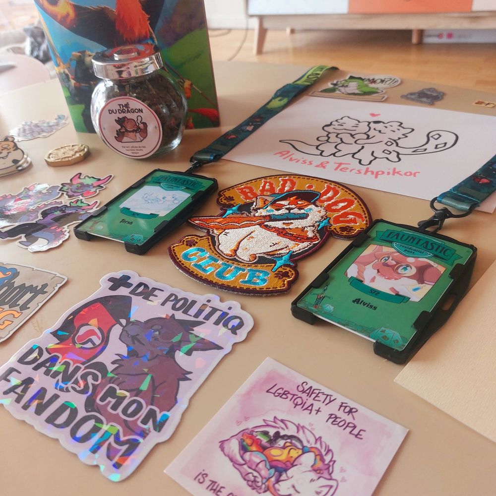 Picture of several objects connected to the furry convention Fauntastic 5.

- Attendee badges with Alviss and Tershpikor on it
- A cloth patch with a tiny dog holding a knife saying "Bad Dog Club"
- Various stickers with different furry characters, or political messages such as "More politic in my fandom" or "Safety for LGBTQIA+ people is the only gay agenda" (or "Short King")
- A sharpy drawing of Tersh and Alviss cuddling
- A jar of tea marked "Dragon's tea" with a drawing of a anthro dragon drinking tea