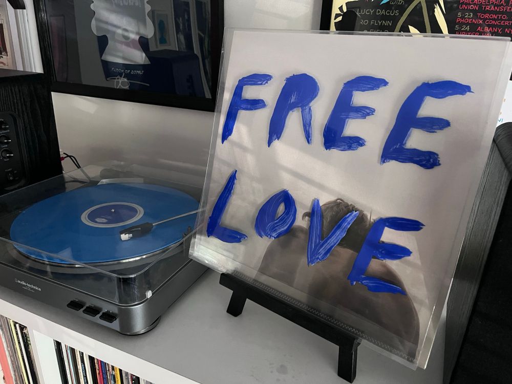 A turntable playing a blue record next to the album cover for the Sylvan Esso album “Free Love”.
