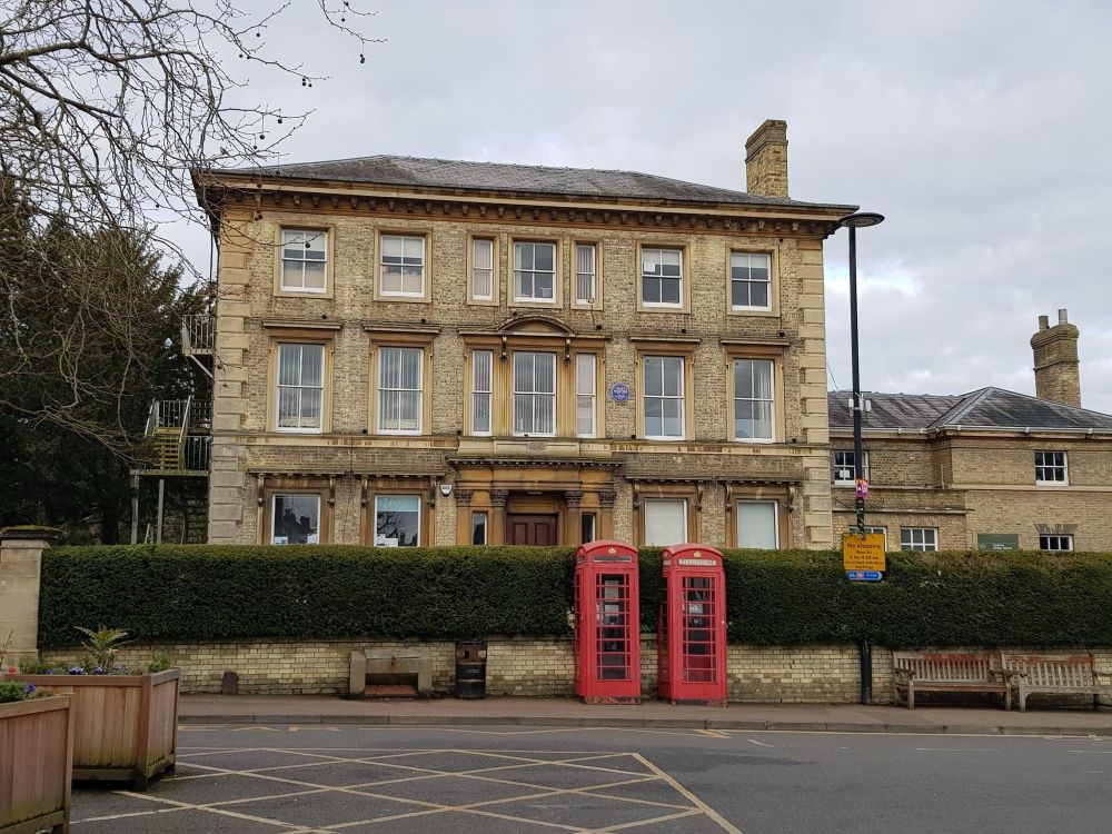 A three storey manor type building, with a hedge and two red phone boxes. 