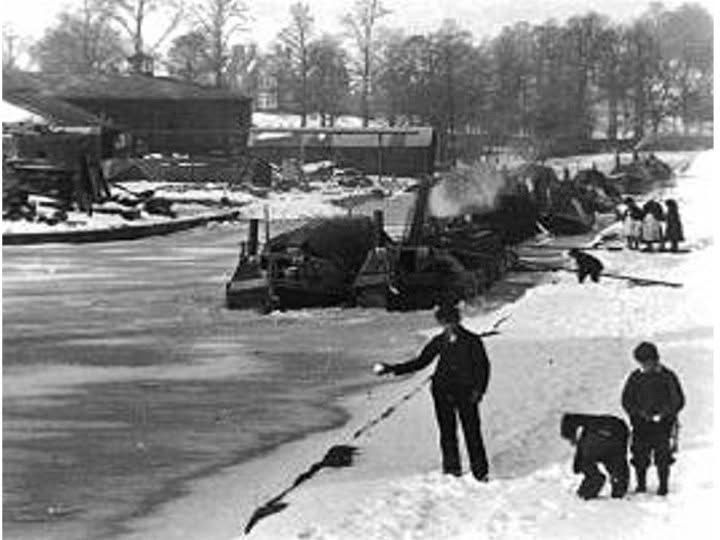 Canal barges trapped in ice on the Grand Union Canal. Boys playing with snowballs and a group of girls probably doing the same. Large house in the background. 