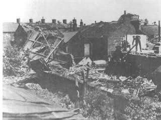 A picture of demolished houses and walls with intact houses in the background.