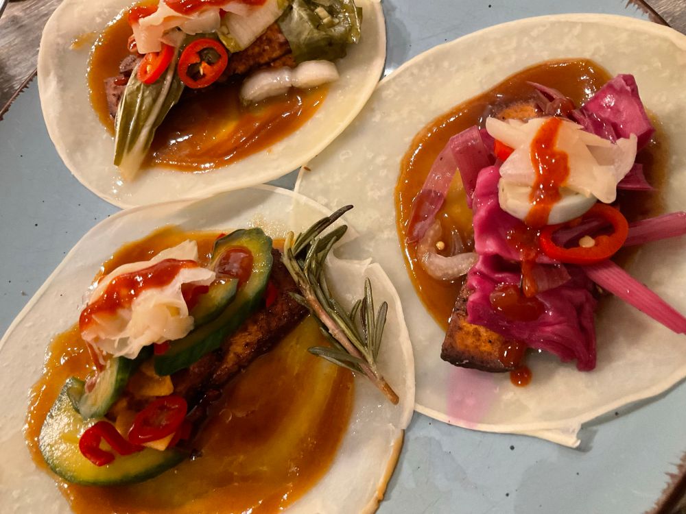Auf einem blauen Teller befinden sich drei Pekingentepfannkuchen(bestehend aus Wasser,Salz,Mehl und Soja Öl).Diese sind mit  Tofu nach Pekingente Art,verschiedenen  sauer süß eingelegten  Leckereien : Asaduke Gurke,Pak Choi,Knoblauch,Rotkohl,Lauch,Chilli und Ingwer.