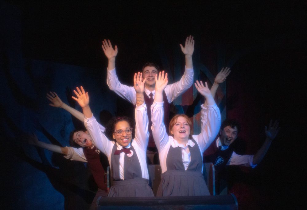 5 actors in Ride the Cyclone creating a rollercoatser ride with their positions. All of their arms in the air and smiling. 