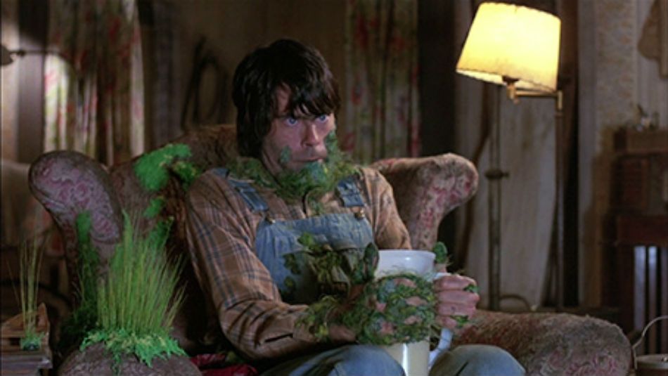 A shot from the film Creepshow, showing a man with plants and moss growing all over his body and living room