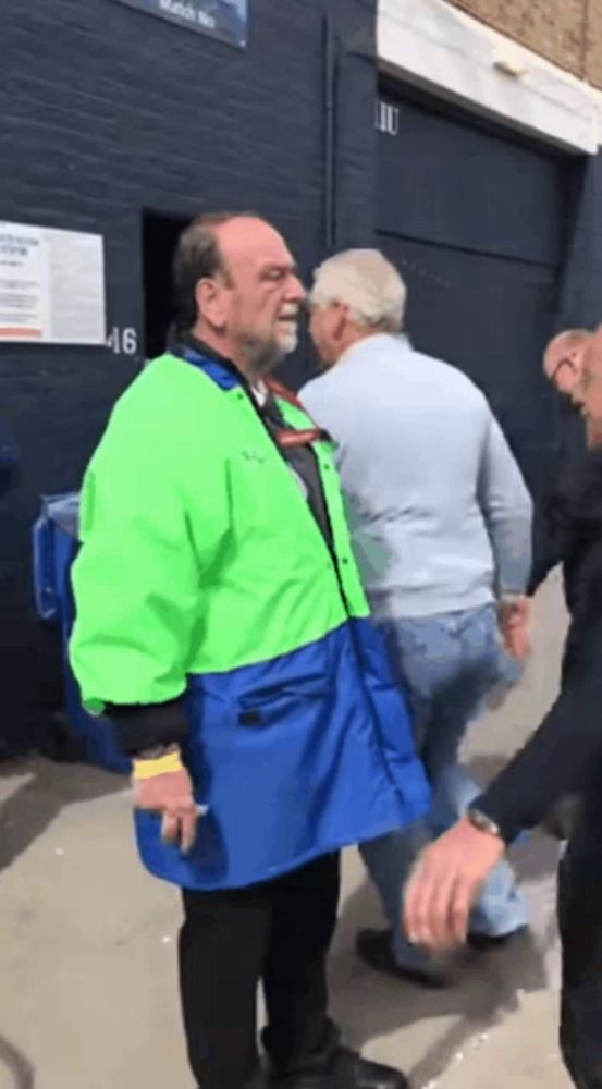 a man in a green and blue jacket stands next to another man