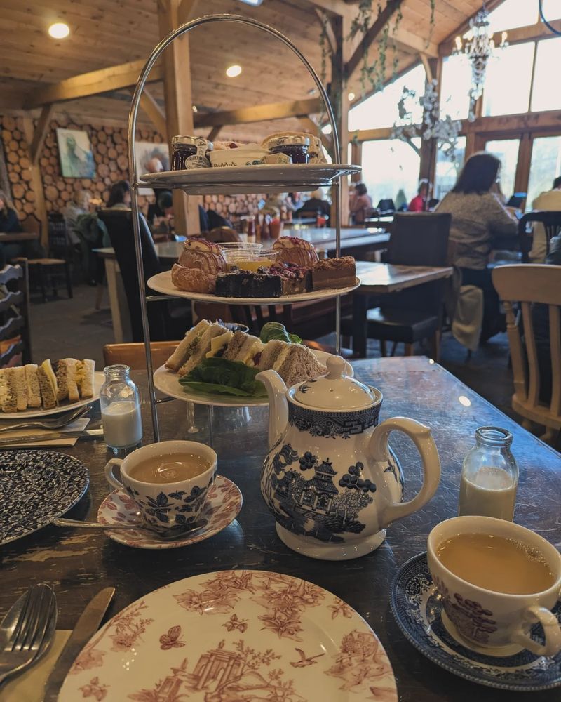 Table with an afternoon tea set up of scones, cakes, and sandwiches as well as a teapot and two cups of tea