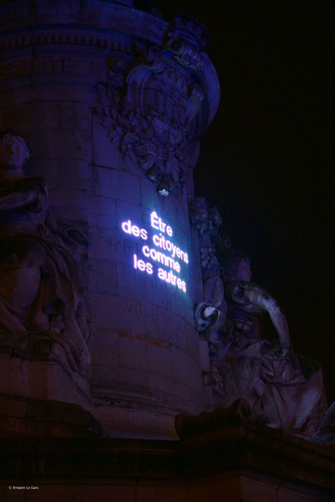 Gros plan sur le socle de la statue de la République. Un texte y est projeté : être des citoyens comme les autres.
