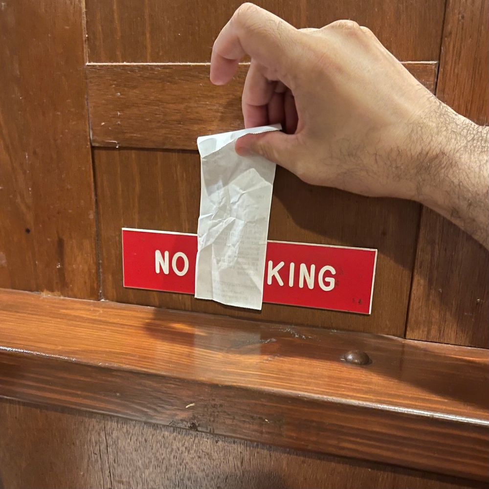 A “no smoking” sign with “smo” part covered with a receipt so that it reads “no king”. Inspired by similar techniques with “no parking anytime” signs 