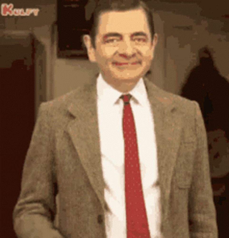 mr bean is wearing a suit and tie and smiling at the camera .