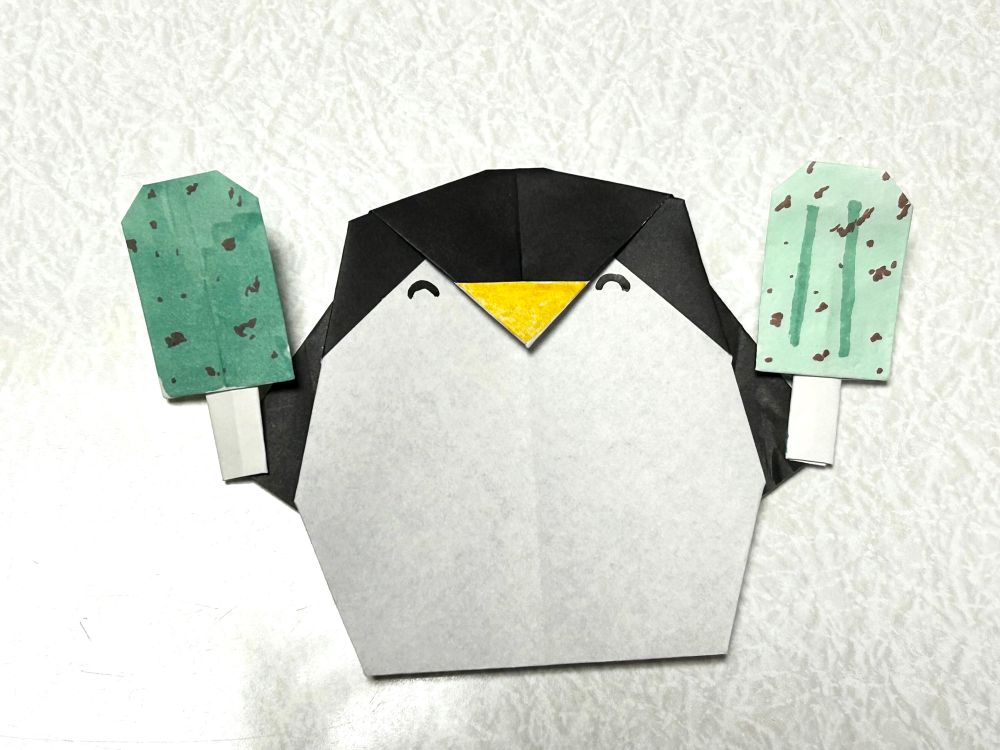 ペンギンの折り紙。両手にそれぞれ違うチョコミントのアイスバーを持ちニコニコ笑っている。