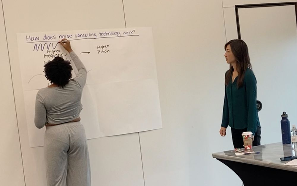 participant recording ideas on a collect and display board to answer the question How does noise cancelling tech work?
