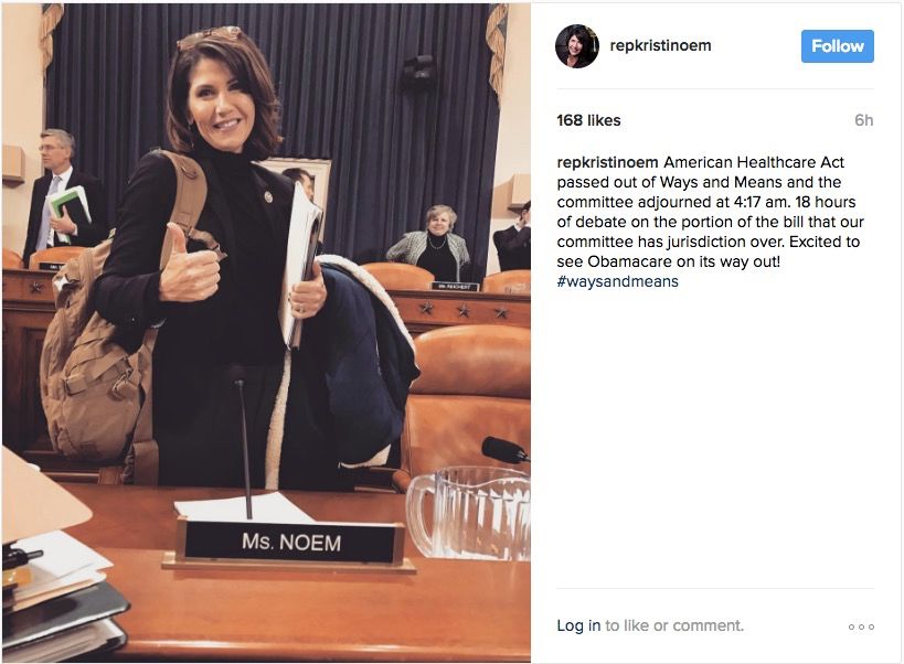 picture of kristi noem in congress in 2016 doing a thumbs  up with a backpack and black turtleneck