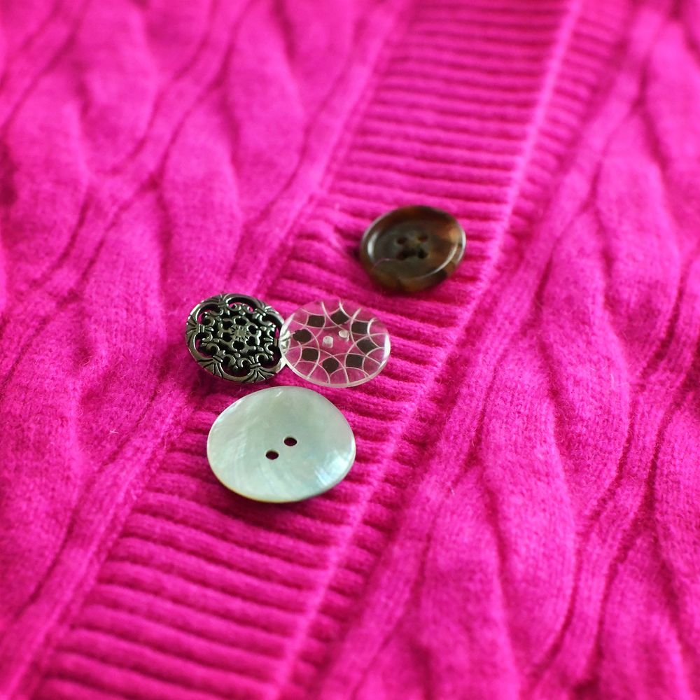close up on the three button options. one is a large white shell button, one is a small pewter button with a floral pattern, one is a glass button with a geometric design