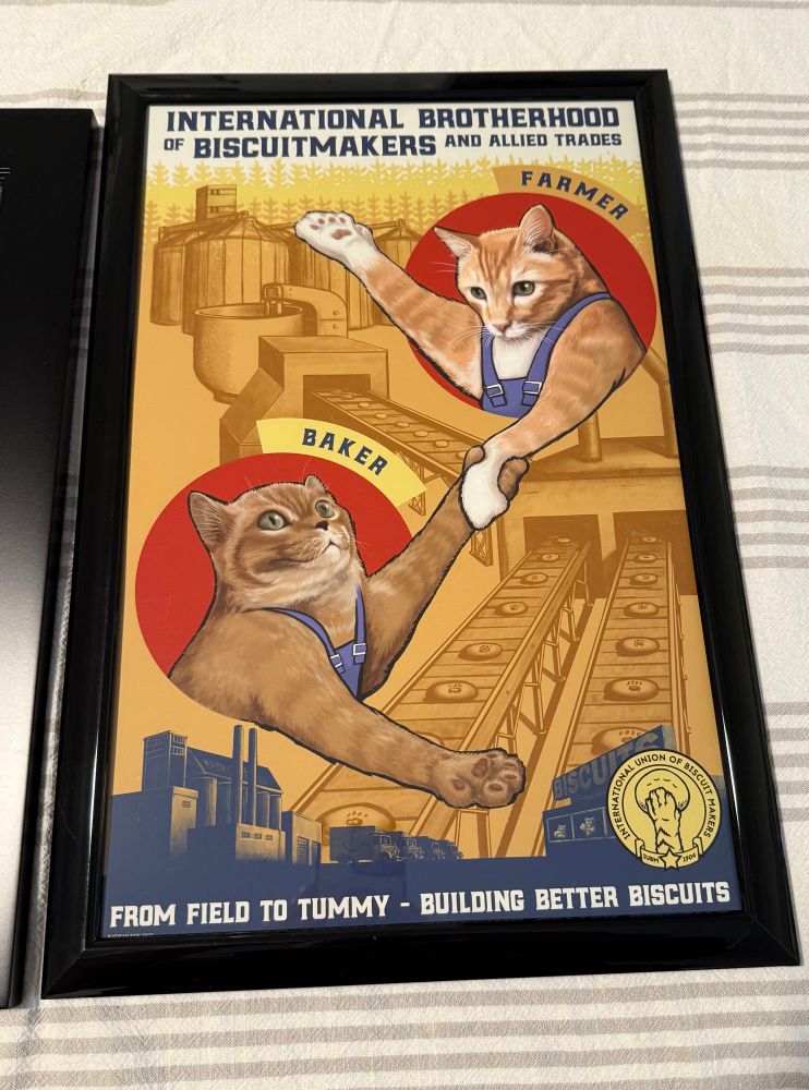 Closeup of the cat poster. A cat labeled “farmer” is joining paws with a cat labeled “baker” under a label that says “International Brotherhood of Biscuitmakers and Allied Trades.” Both cats are wearing overalls, and in the background are two converter belts carrying biscuits with a paw print in each one. Underneath it says, “From field to tummy — building better biscuits.”