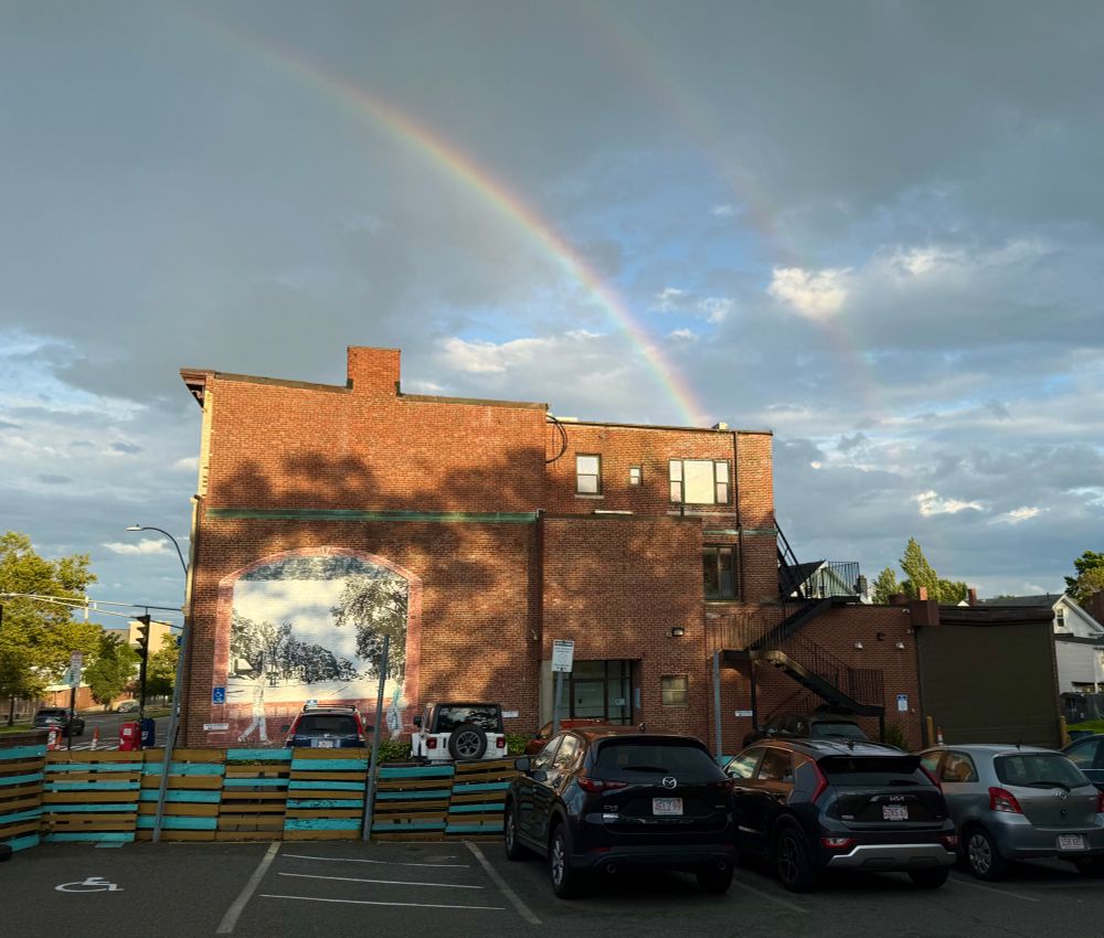 A view of just the brick building, where the rainbow has gotten brighter and second, fainter rainbow has appeared above it. The order of the colors appears reversed in the upper rainbow. 