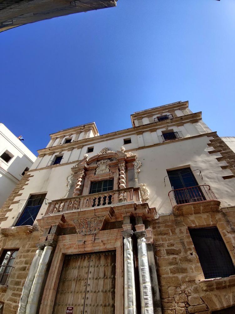 An 18th century house owned by a merchant. A grand door surrounded by columns support a first floor balcony of the door. 

The ground floor was used for storage of goods, the merchant's family lived on the first floor, the servants on the second and the towers on top were used to keep a lookout, and communicate with, incoming ships bringing goods into Cadiz

Most merchant houses in Cadiz have been converted into hotels but developers are required to preserve their architectural features 