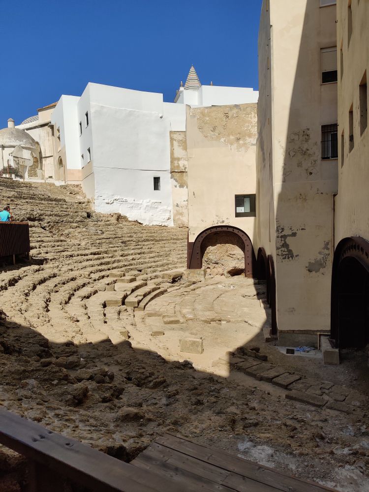 A 1/3 of the semicircle that was created by the terraced seating facing the stage. Metal arches support the residential buildings which are built on top of what was the stage. The theatre was built from stone taken from the seabed at low tide. Later the same stone bricks were recycled by the Moors and then the Spanish in the 18th century to build Cadiz old town.